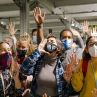 A group of masked young activists gathered round the camera. They're energetic and animated, with hands raised or cupped to their mouths as they chant slogans.