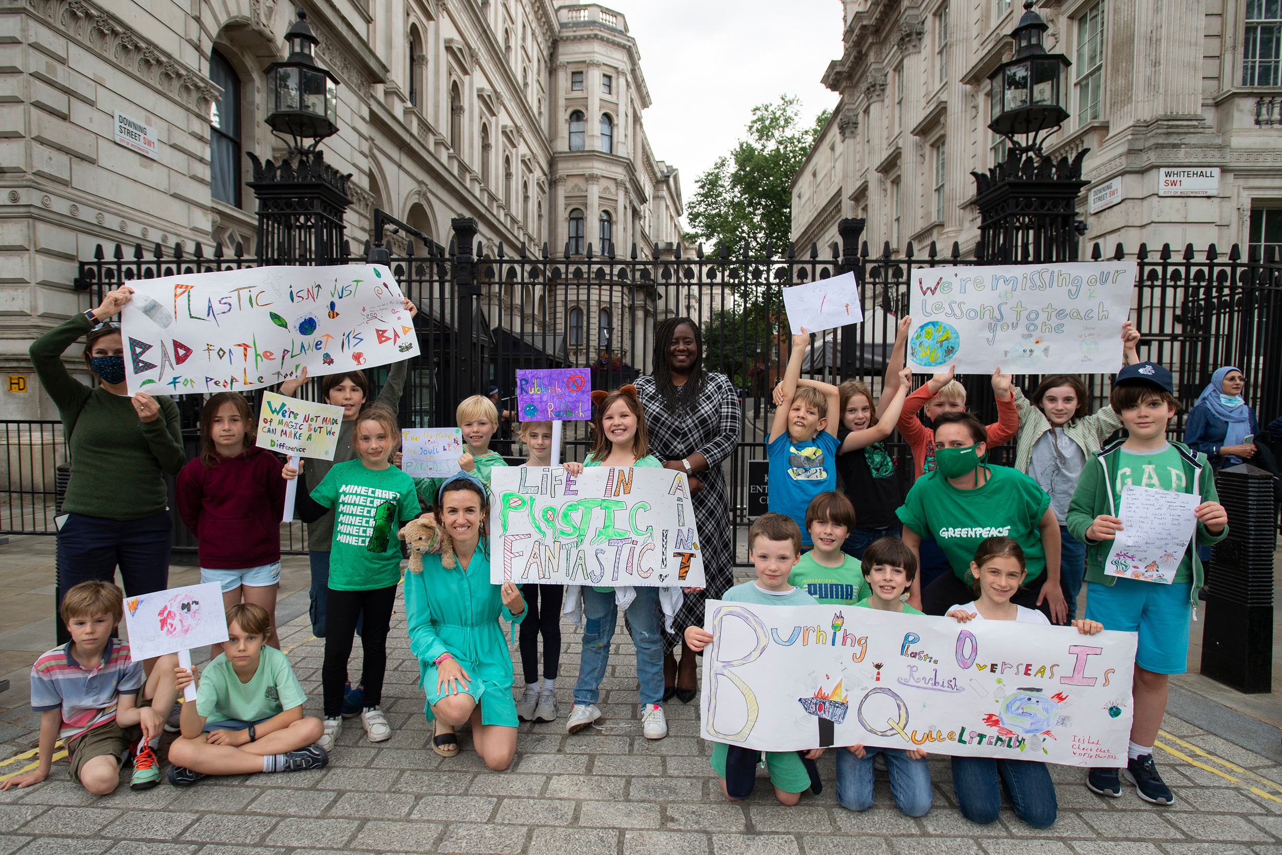 A large group of children stand in front of the railings of Downing Street holding colourful hand-drawn signs calling for an end to plastic waste exports.