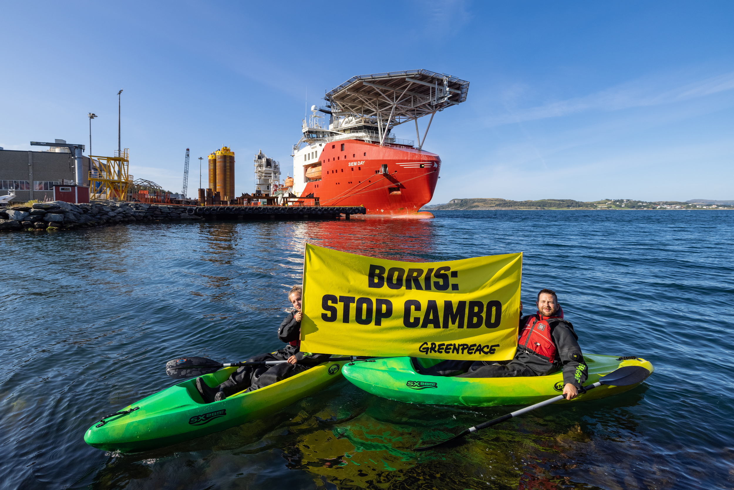 Two people in kayaks hold up a sign reading "Boris: Stop Cambo". Behind them is a massive ship with large equipment for an off-shore rig.