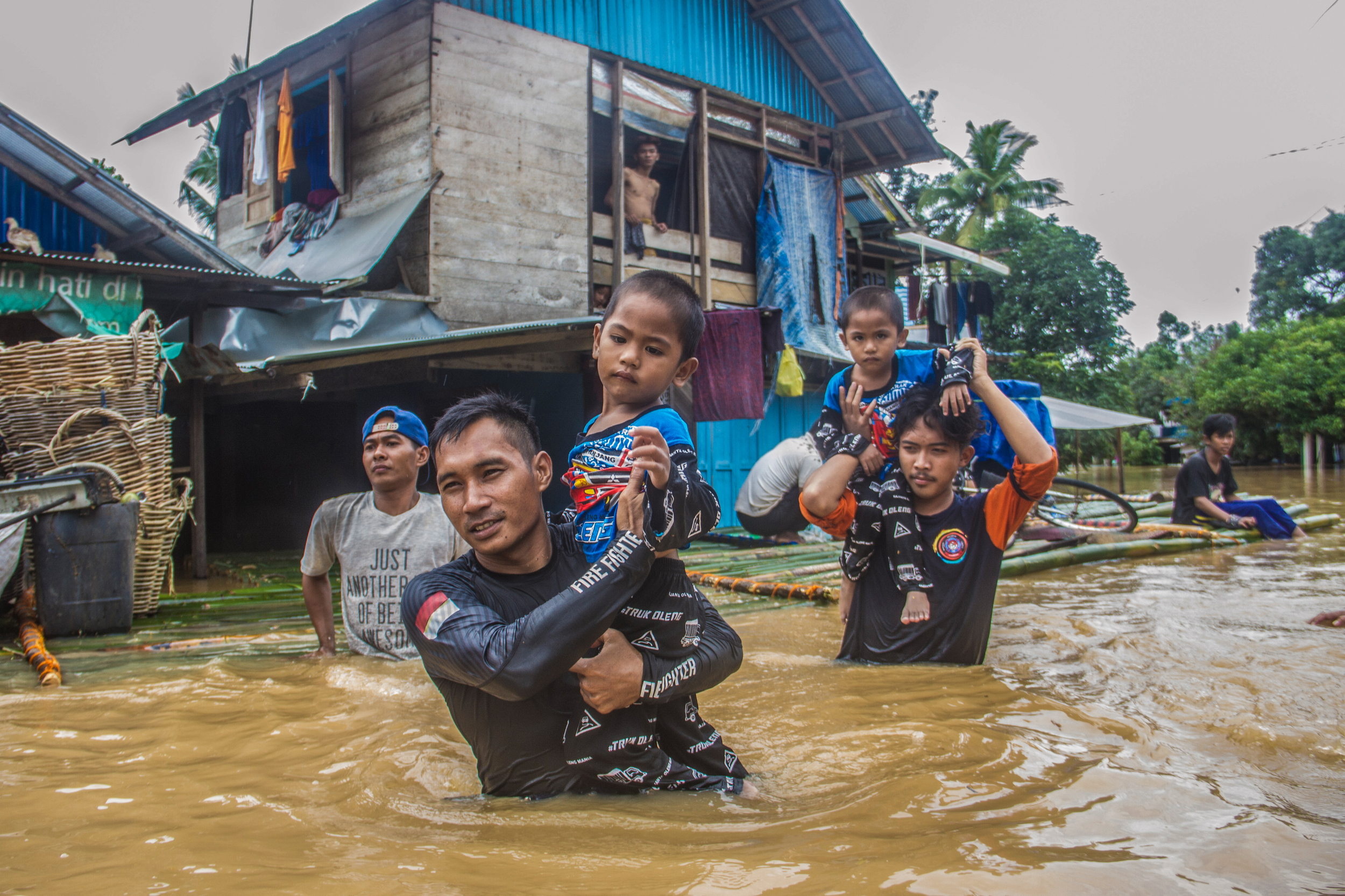 Two men carry small children through chest-deep flood water.