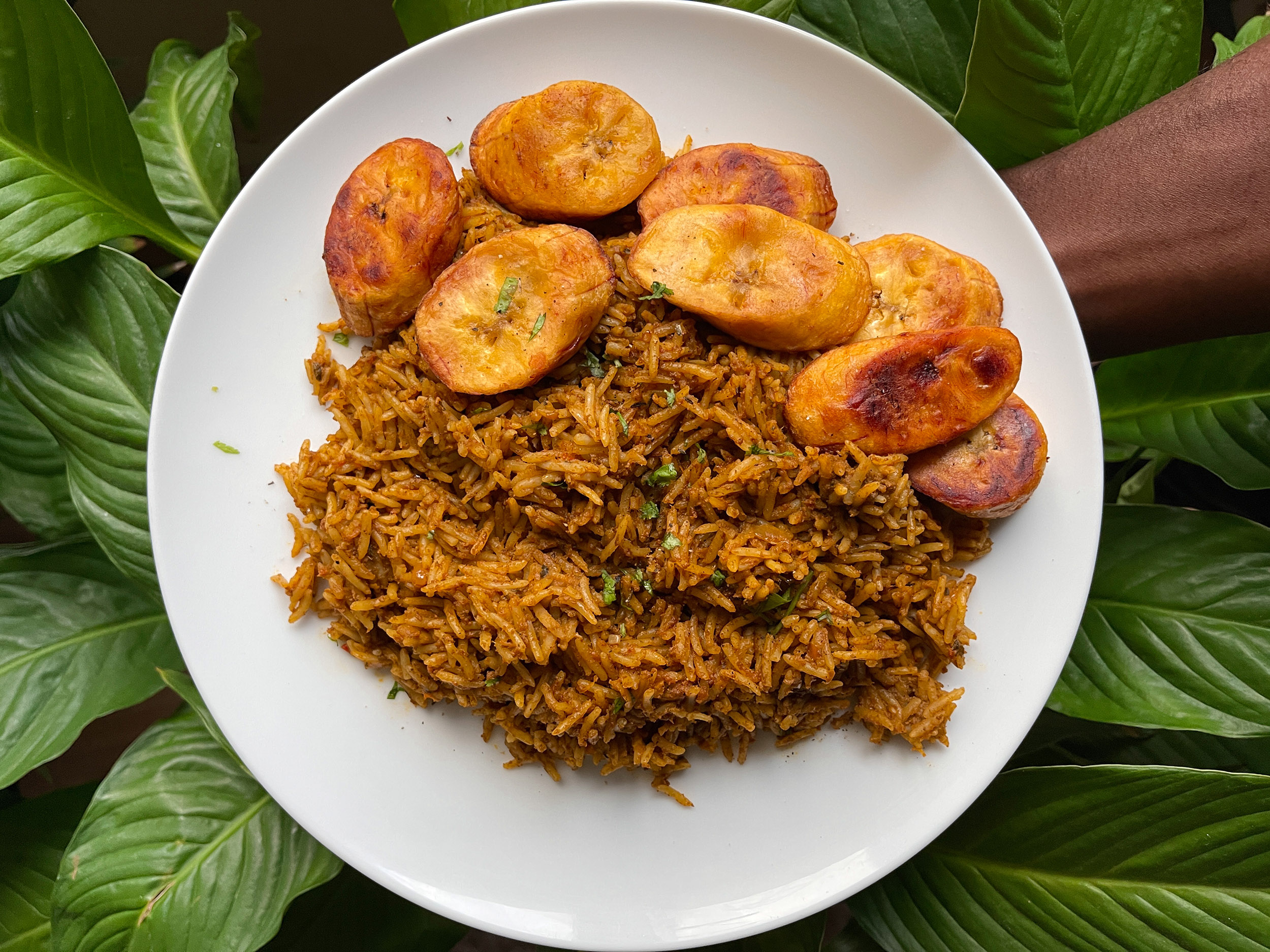 A beautifully presented plate of banga rice with fried plantain, against a background of lush green leaves.