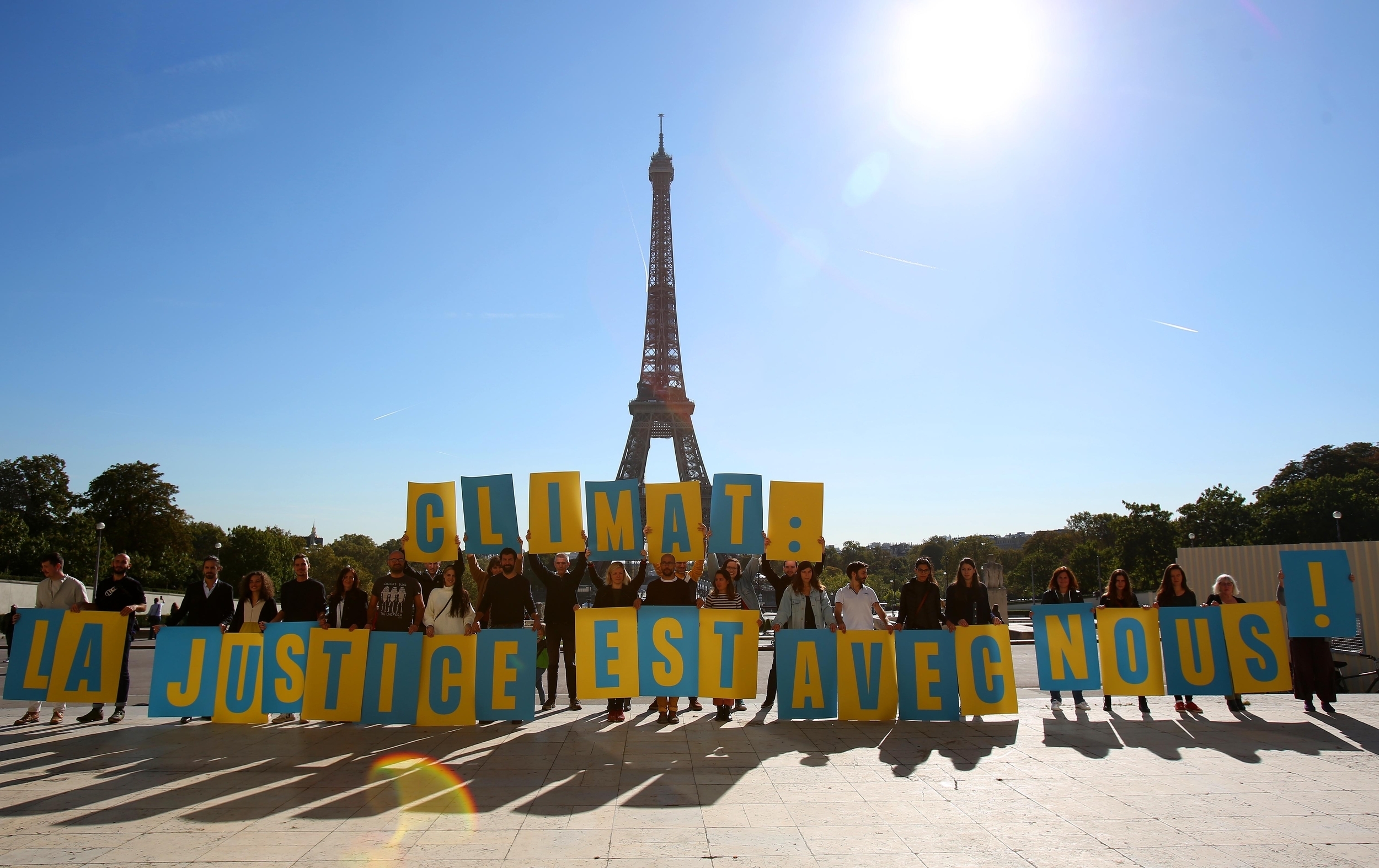 A large group of people in front of the Eiffel Tower hold up blue and yellow signs spelling out 'Climat: la justice est avec nous'