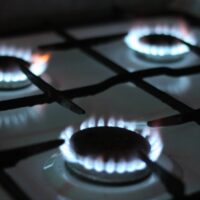 On a home stovetop, three gas burners emit rings of blue flame