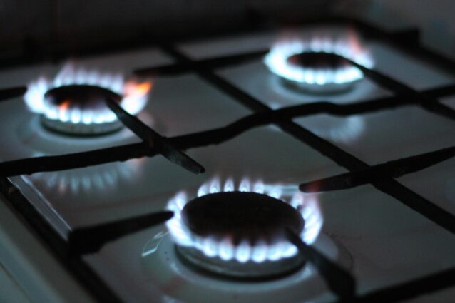 On a home stovetop, three gas burners emit rings of blue flame