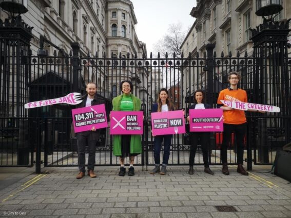 Campaigners stand at the gates to Downing Street holding bright pink placards calling for a ban on the most harmful single use plastics.