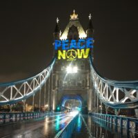 The words 'Peace now' in the blue and yellow colours of the Ukrainian flag, projected onto Tower Bridge at night