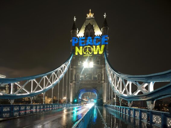 The words 'Peace now' in the blue and yellow colours of the Ukrainian flag, projected onto Tower Bridge at night
