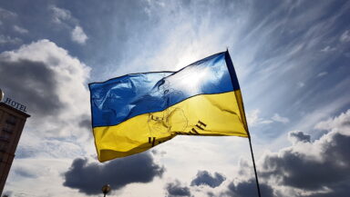 The Ukrainian blue-and-yellow flag, backlight by the sun against a blue sky with a few clouds
