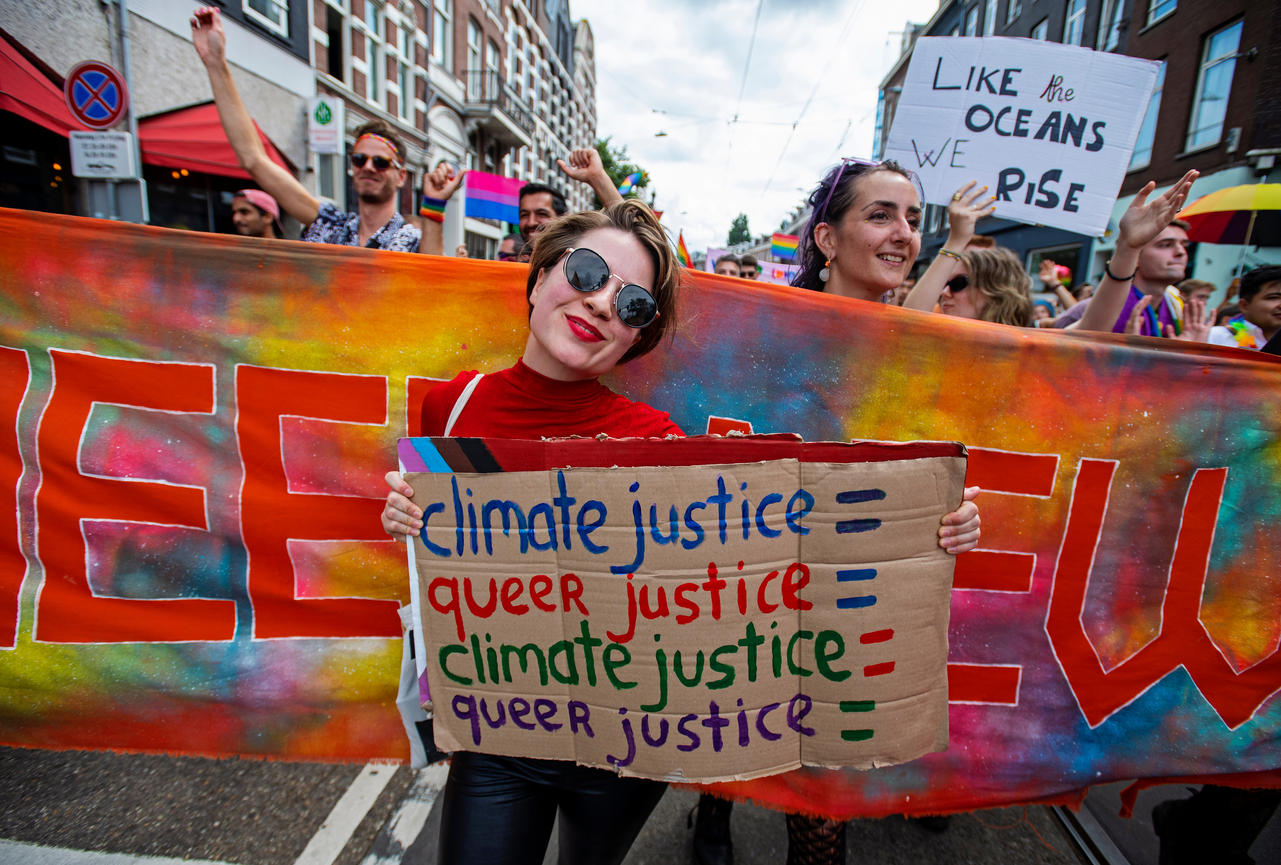 Person at a pride march holds a sign saying 'Climate justice = queer justice'