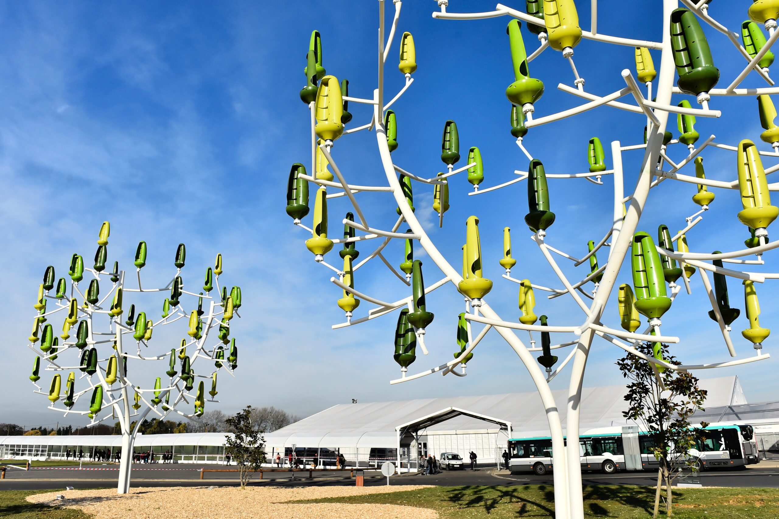 White tree structures, with yellow and green ‘leaves’ which look like upturned plastic bottles with holes to capture wind.
