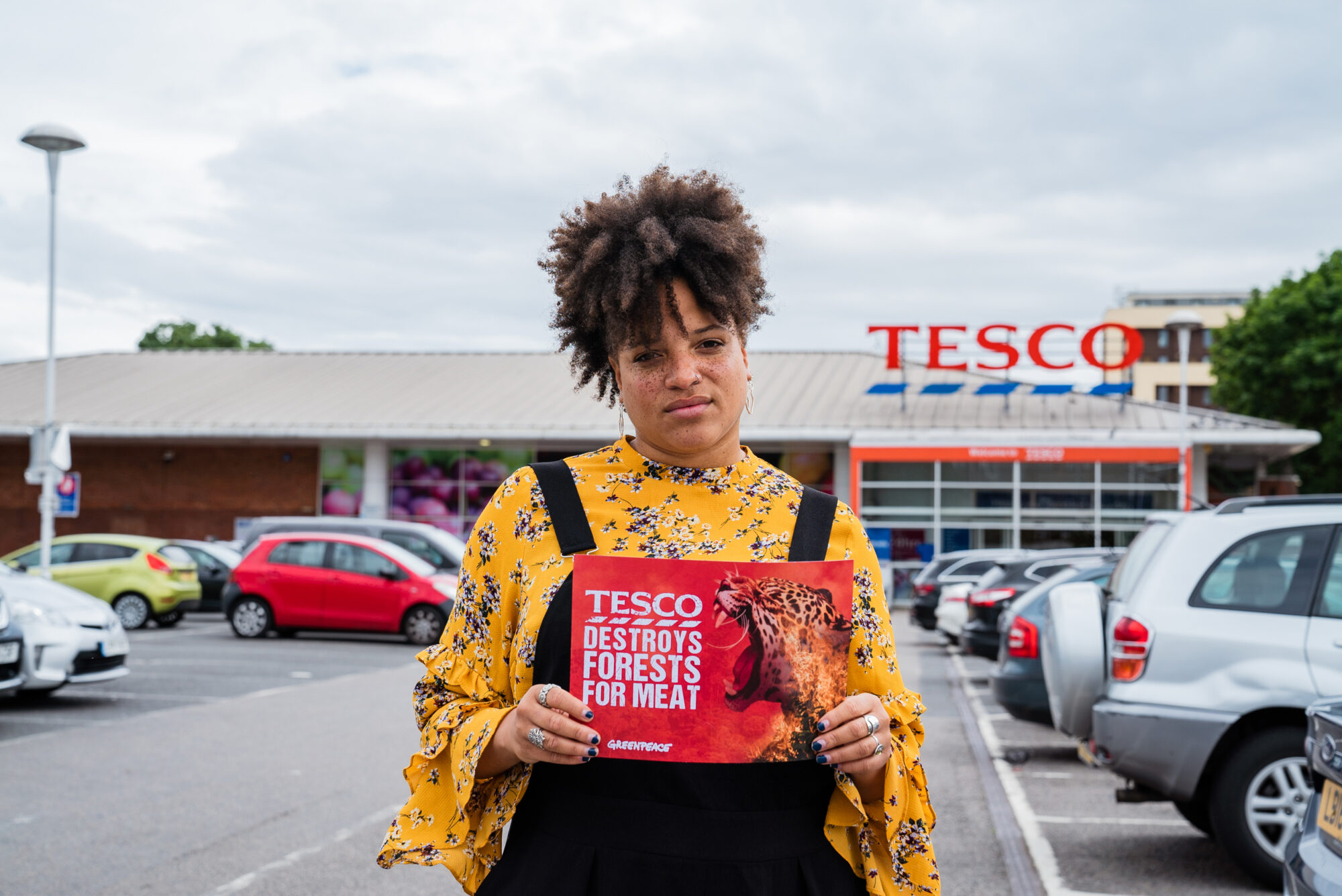 Laya Lewis stands outside the supermarket, Tesco, holding a sign that says "Tesco destroys forests for meat"