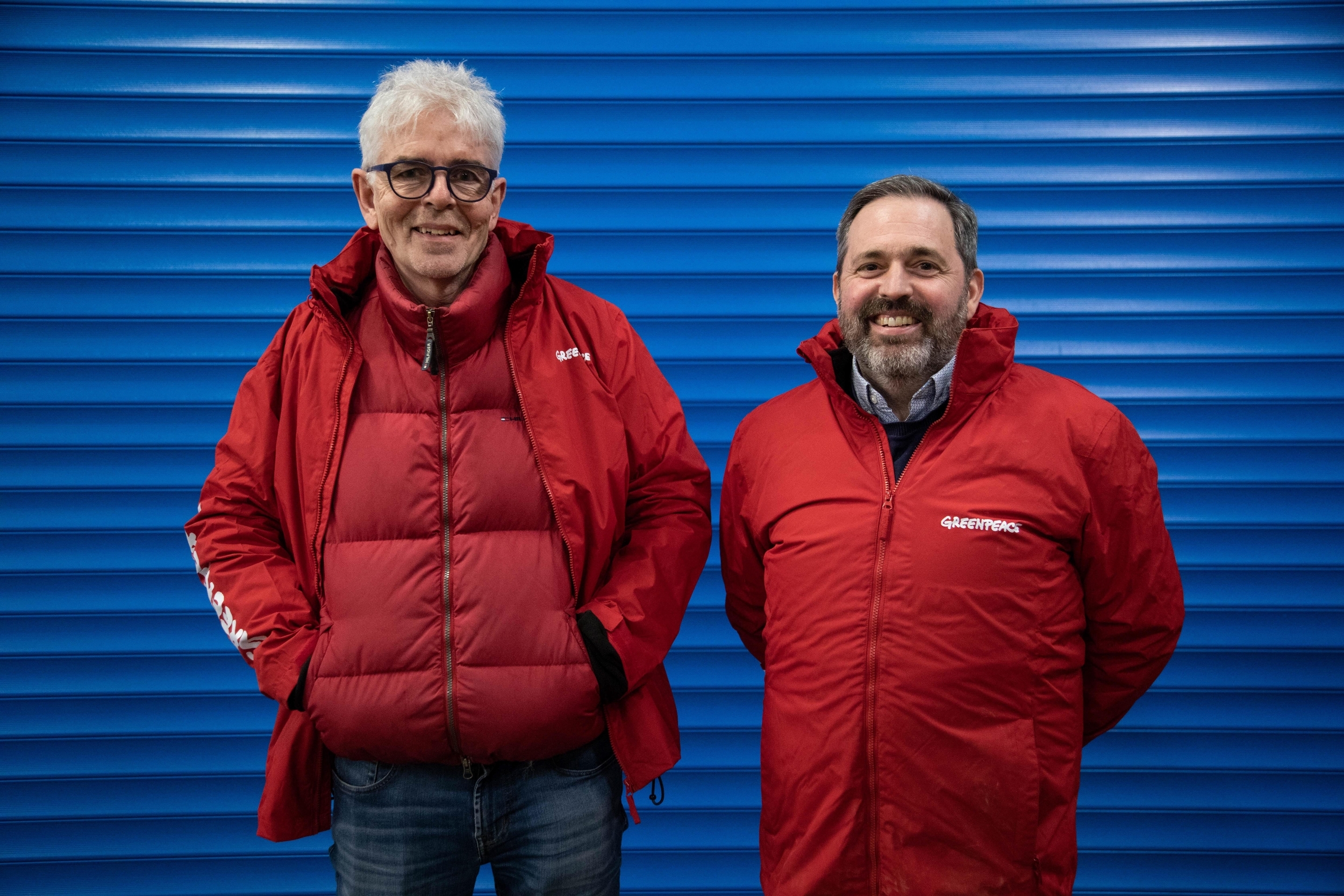 John Sauven with Pat Venditti, Greenpeace UK. The two men stand in bright red jackets against a deep blue background.