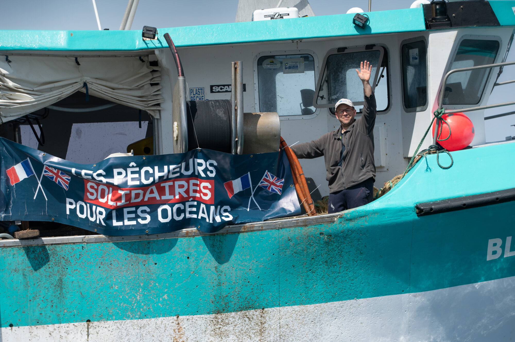 French fisherman on his boat with a banner that says "Les pêcheurs solidaires pour les oceans". In English this means "Fishermen solidarity for the oceans"