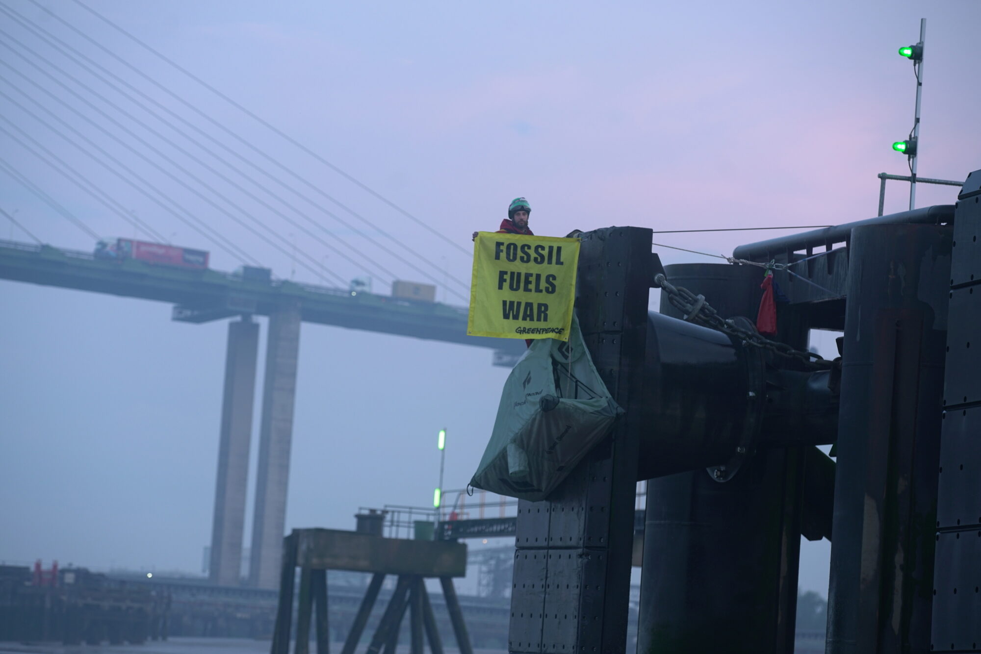 Activist sits on a dock holding an oil fuels war banner