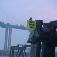 Activist sits on a dock holding an oil fuels war banner