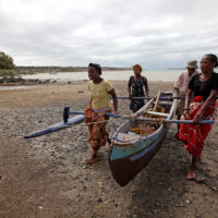A group of people carrying a traditional wooden fishing boat up a beach