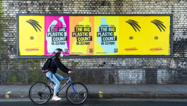 A person on a bike rides past colourful billboards advertising the Big Plastic Count