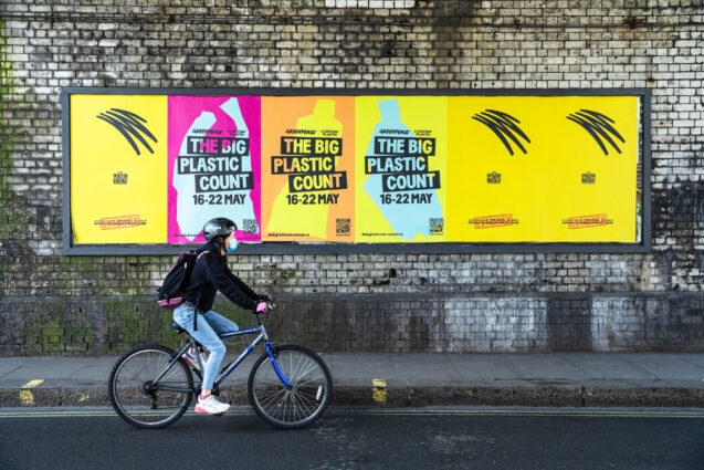 A person on a bike rides past colourful billboards advertising the Big Plastic Count