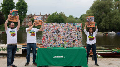 Three volunteers wearing branded tshirts stand around a street stall holding up campaign merchandise.