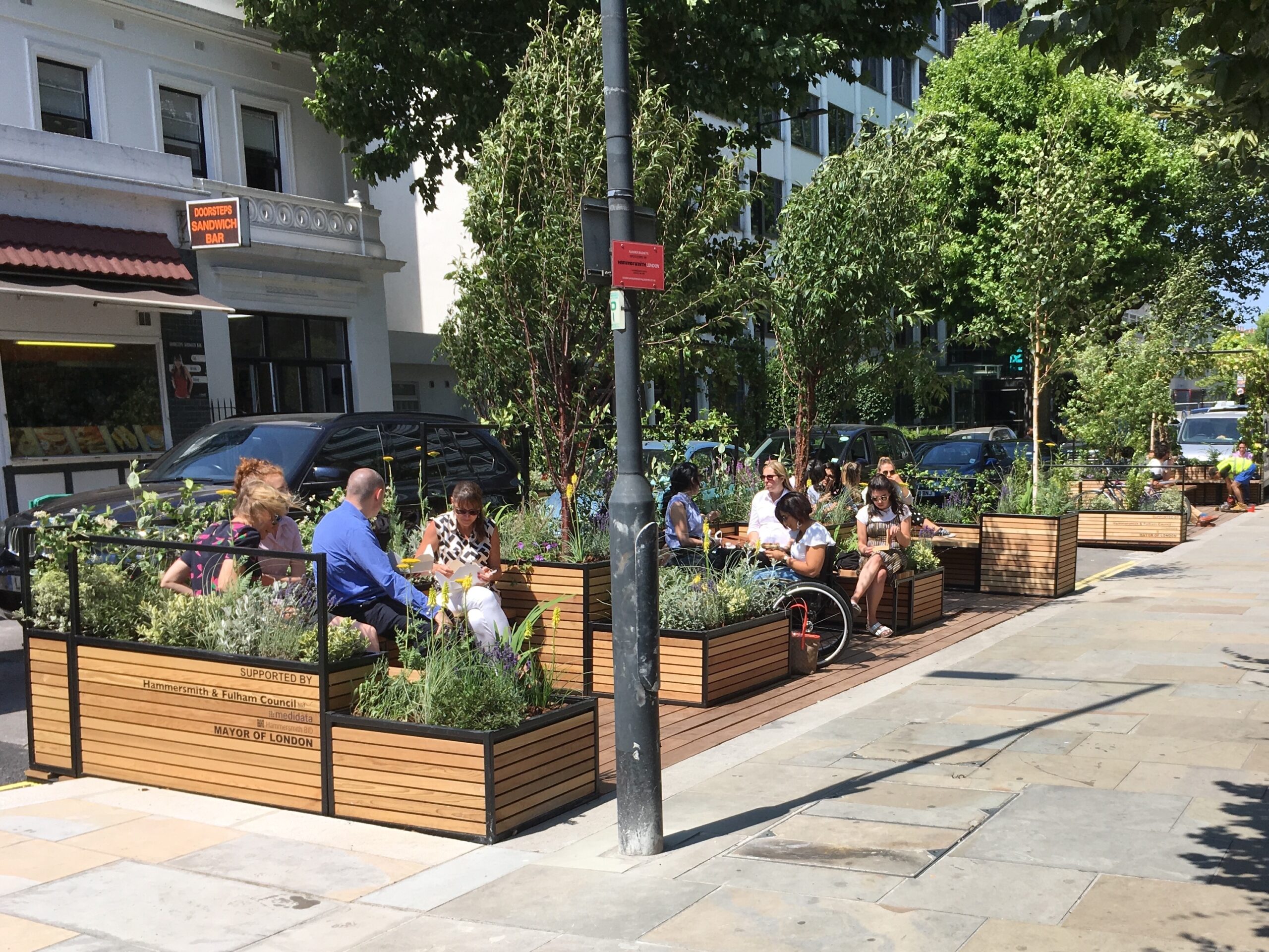 People sit in a small space with plant boxes in the middle of a city street.