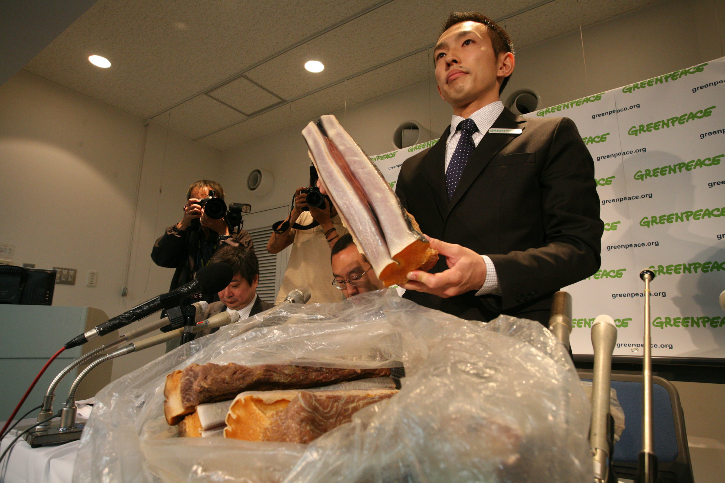 A man holding a large slice of whale meat with more meat in a bag on the table in front of him