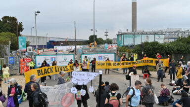 A loose crowd gathered outside the gates to an industrial facility. Large banners read 'Black lives matter' and 'Stop the Edmonton Incinerator'.