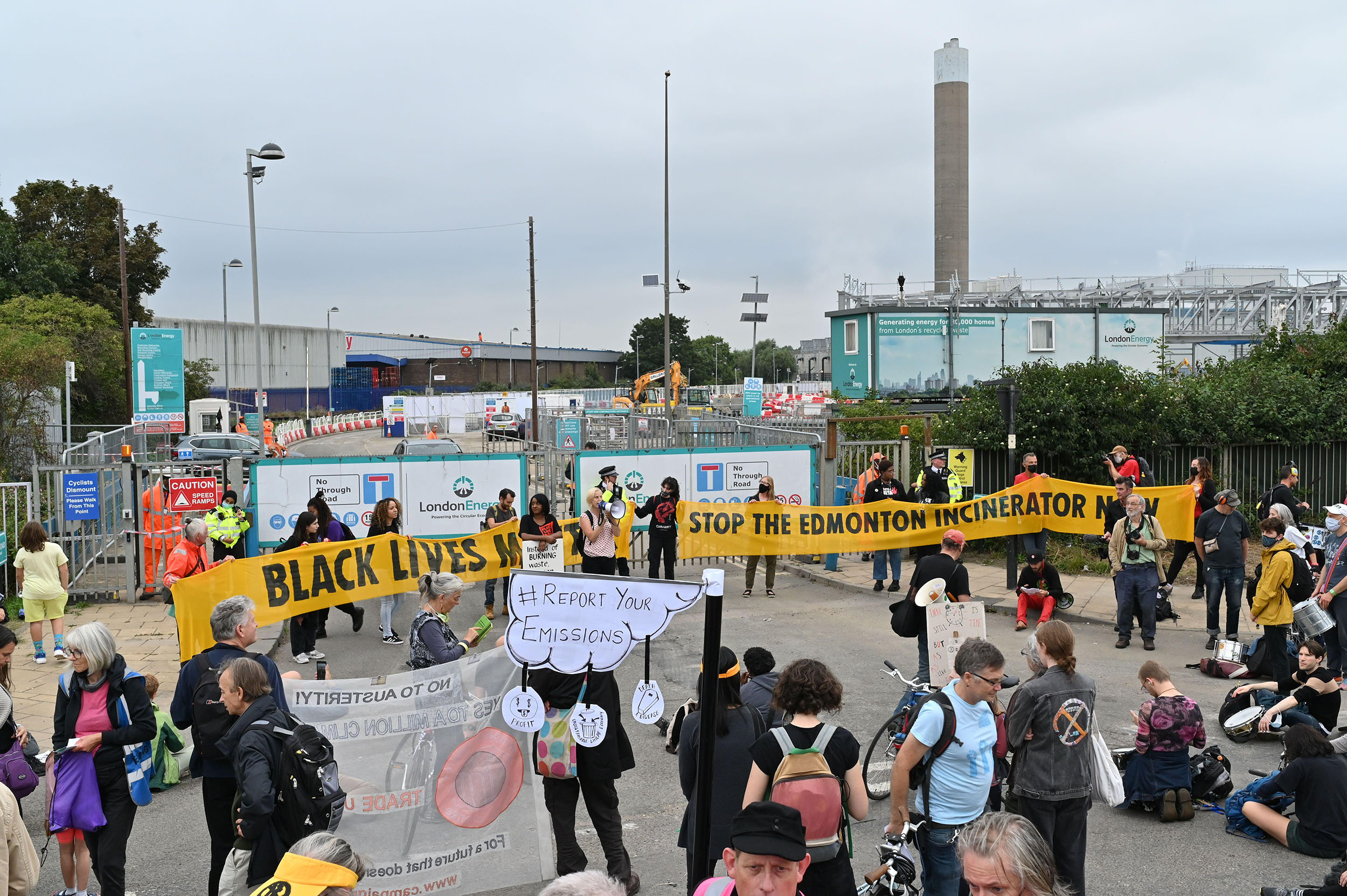 A loose crowd gathered outside the gates to an industrial facility. Large banners read 'Black lives matter' and 'Stop the Edmonton Incinerator'.