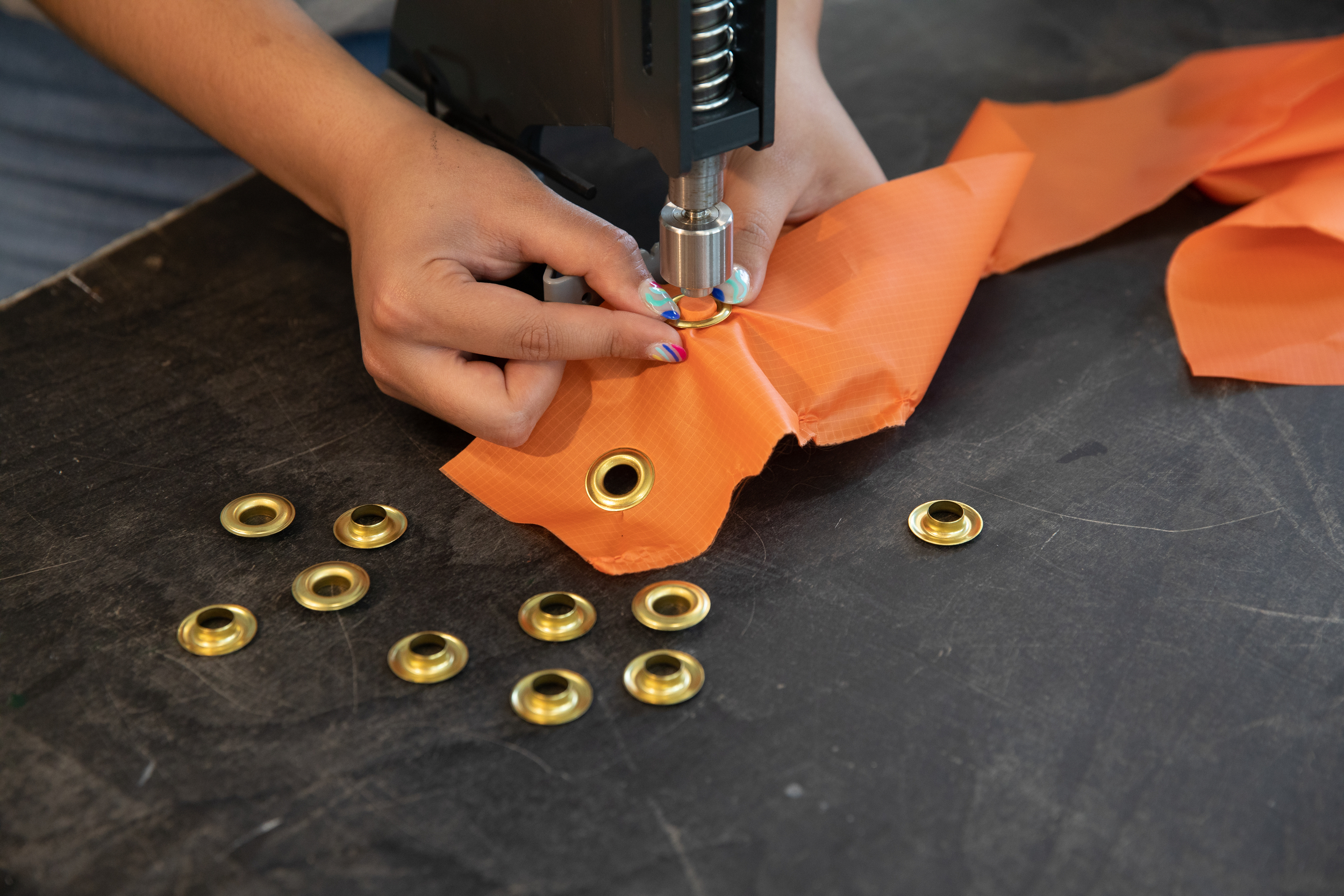 Hands adding eyelets to a piece of orange fabric using a special punch