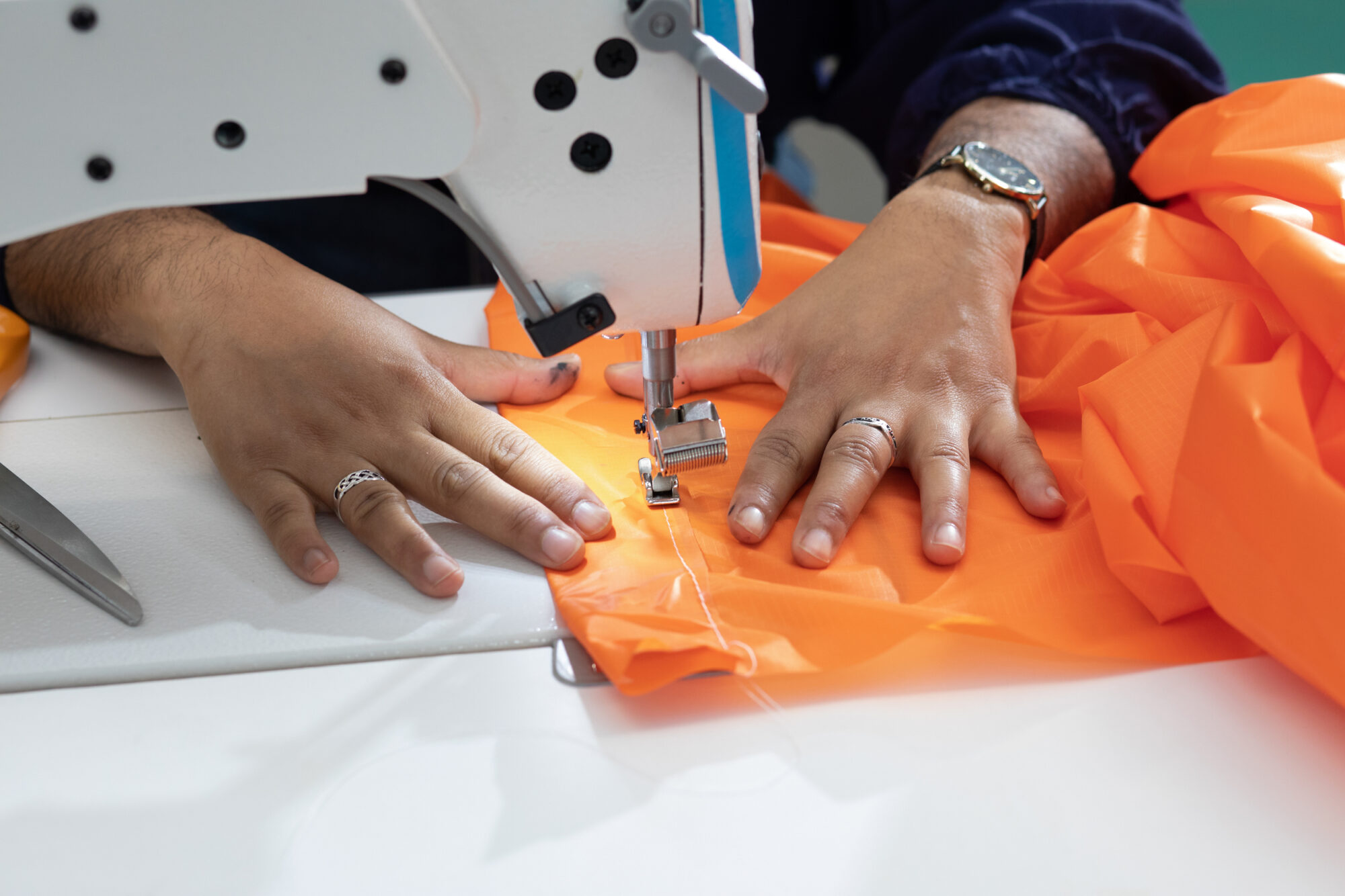 Hands guide a piece of orange fabric under a sewing machine