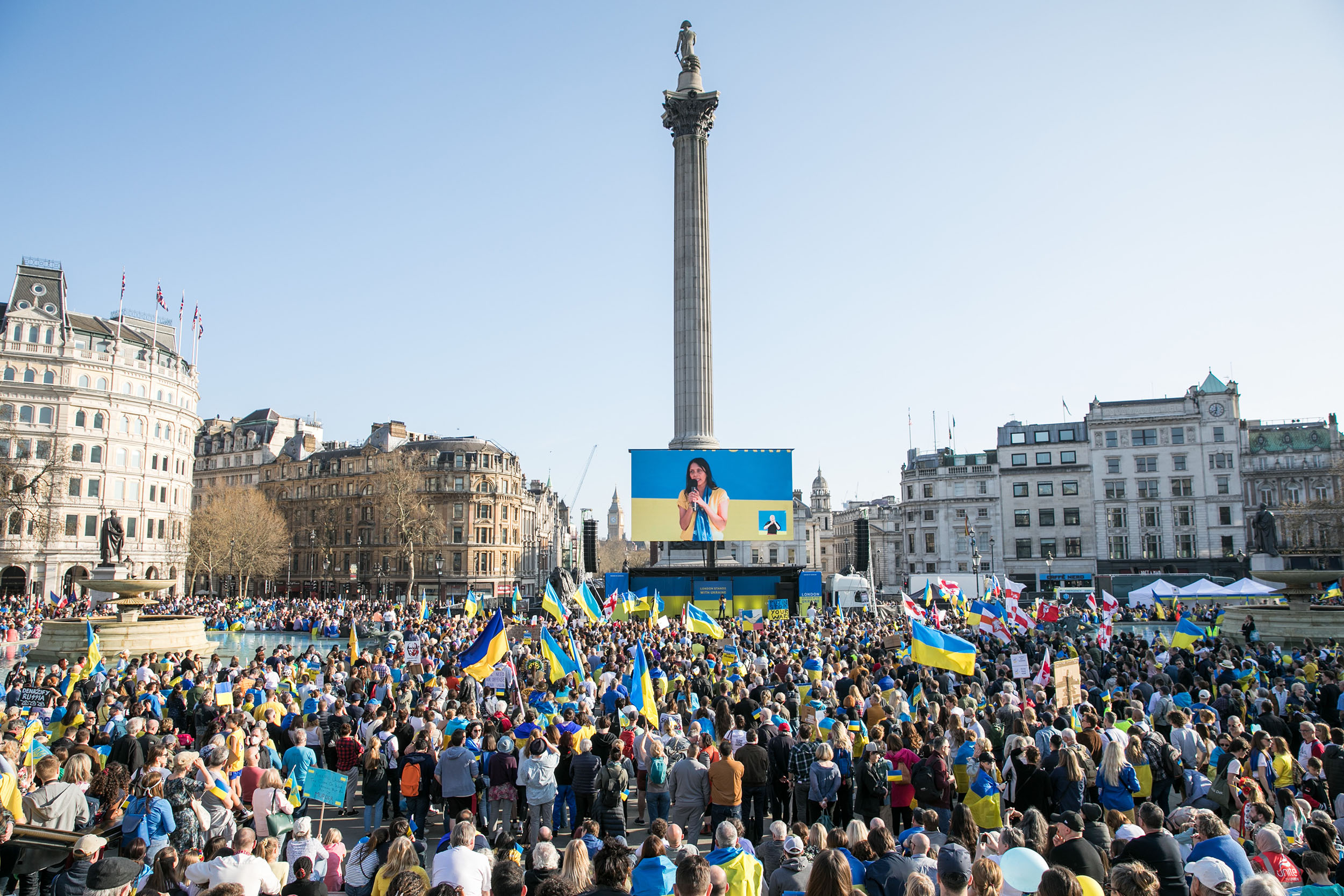 A large crowd gathers in central London to hear Halima Begum's speech. Her face is broadcast to the crowd on a large screen above the stage.A large crowd gathers in central London to hear Halima Begum's speech. Her face is broadcast to the crowd on a large screen above the stage.