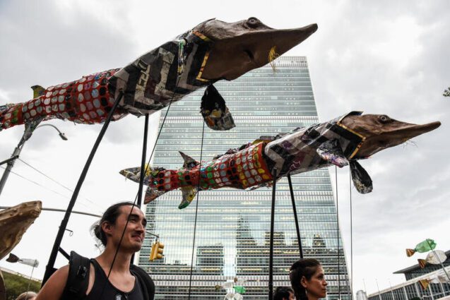 People with fish-like sculptures protest by a large skyscraper