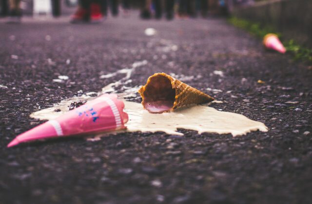 A melted ice cream cone lies on a paved road