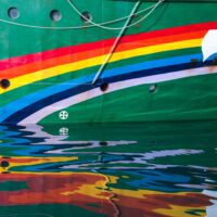 The rainbow insignia painted across the bow of a Greenpeace ship reflects in gently rippling water.