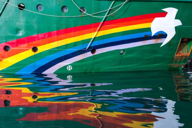 The rainbow insignia painted across the bow of a Greenpeace ship reflects in gently rippling water.