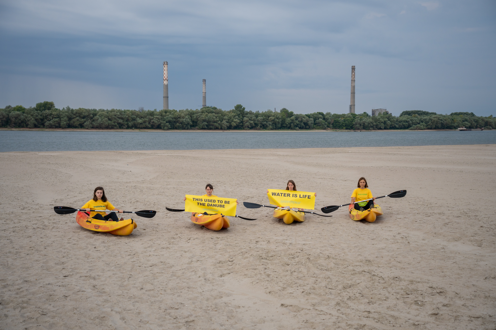 Four campaigners in kayaks on a dry river bank. Their signs read "This used to be the Danube" and "Water is life"
