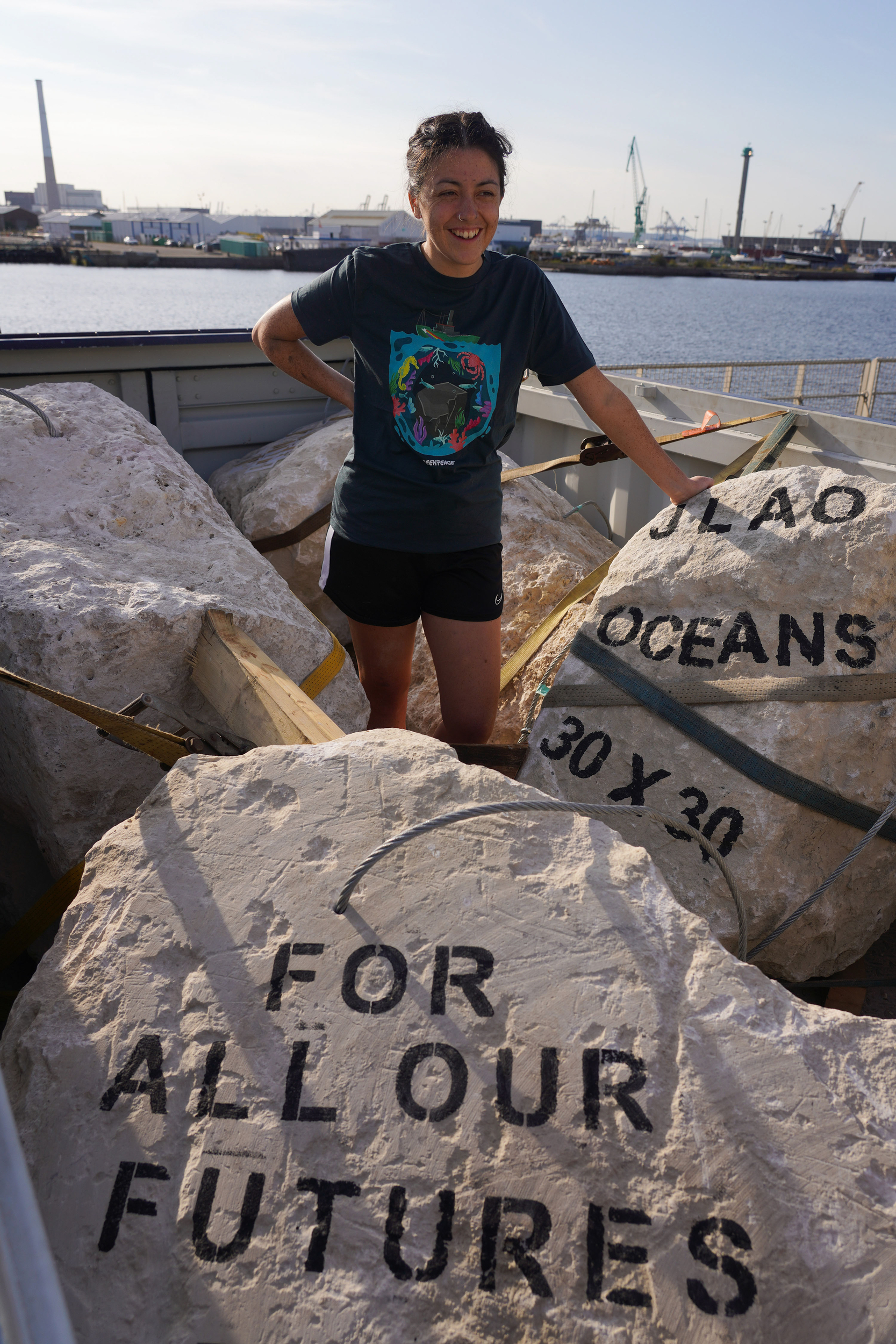 Person standing by stencilled boulders. The front boulder reads "For all our futures". The other boulder with visible writing reads "Oceans 30 x 30"