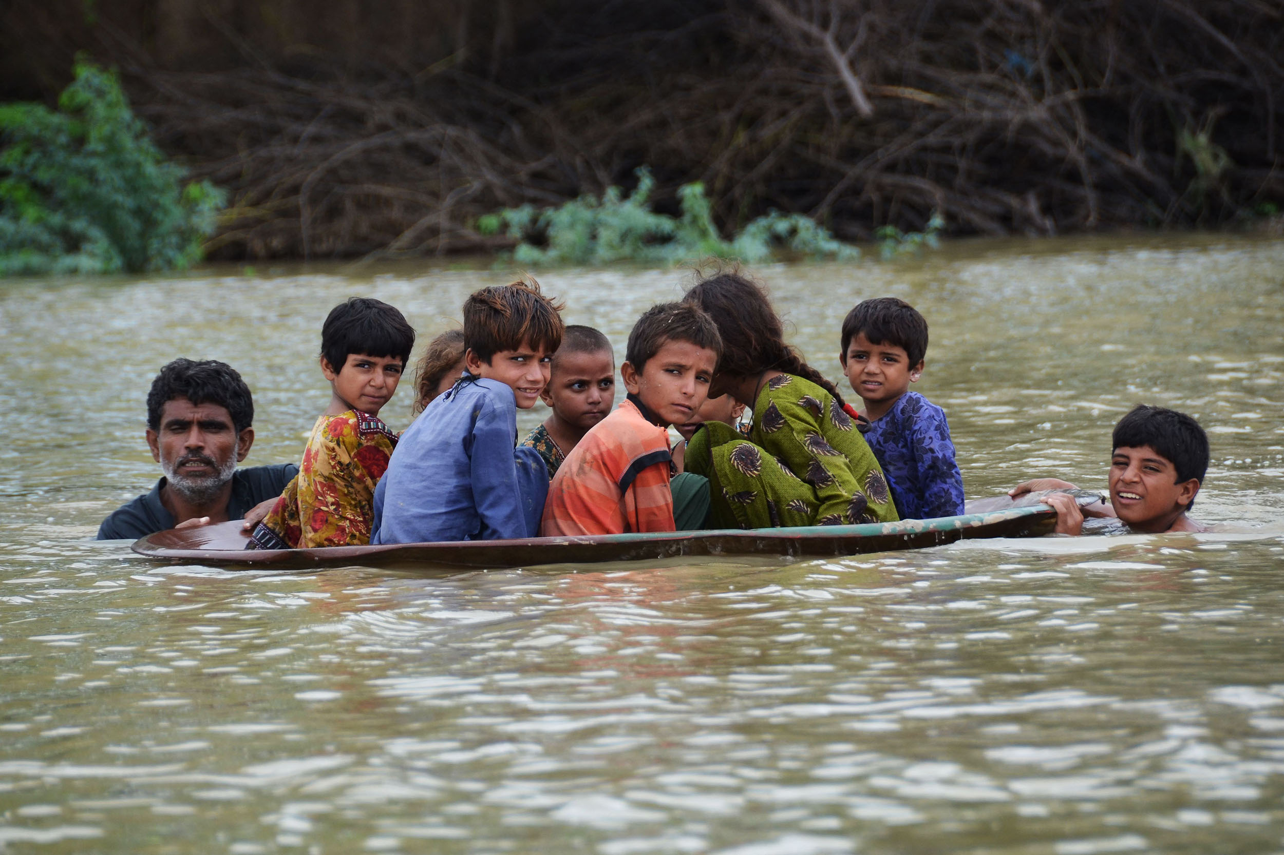 Children get pushed along water in a makeshift boat