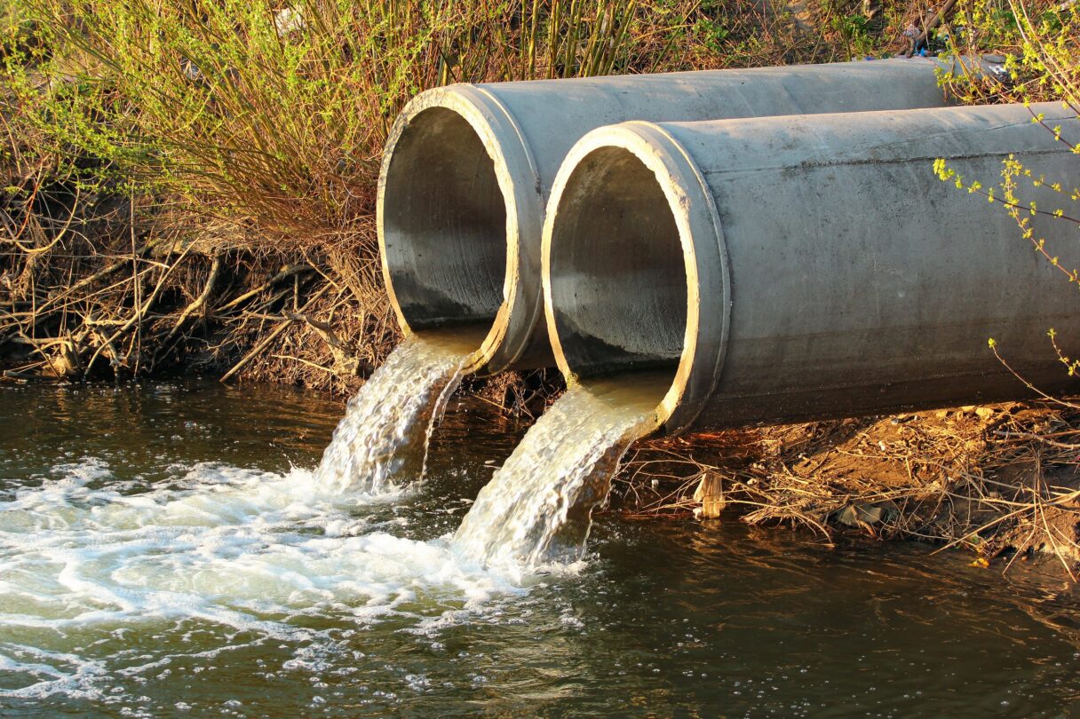Sewage flows into a river from two concrete pipes