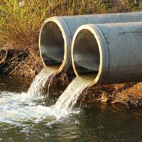 Sewage flows into a river from two concrete pipes