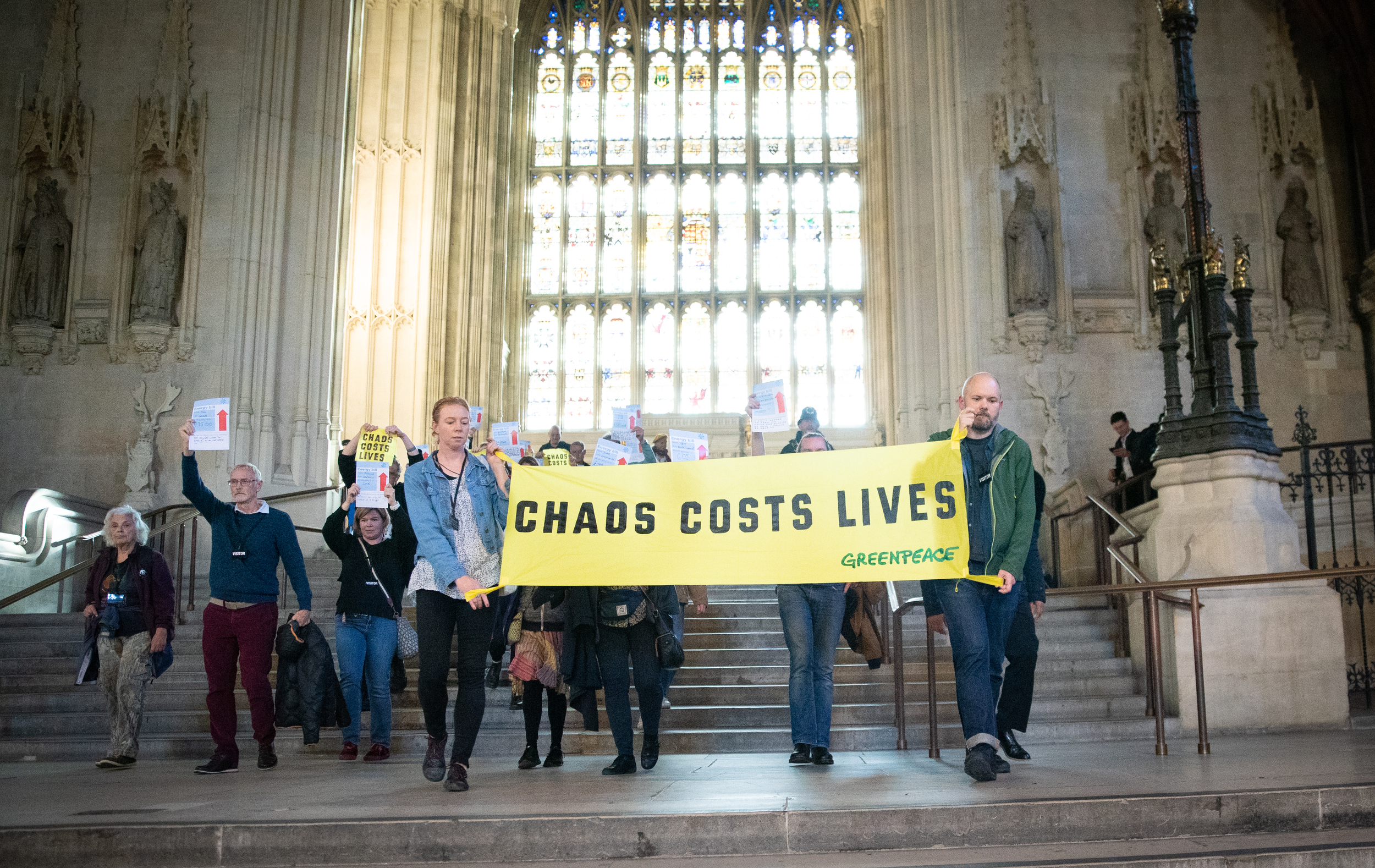 Group of activists hold a banner reading 'Chaos costs lives' in front of an elaborate stained glass window in the Palace of Westminster