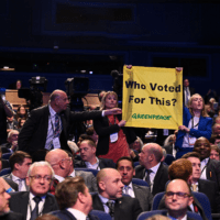 In the audience at the Conservative Party Conference, wo activists hold up a Greenpeace-branded banner reading "Who voted for this?""
