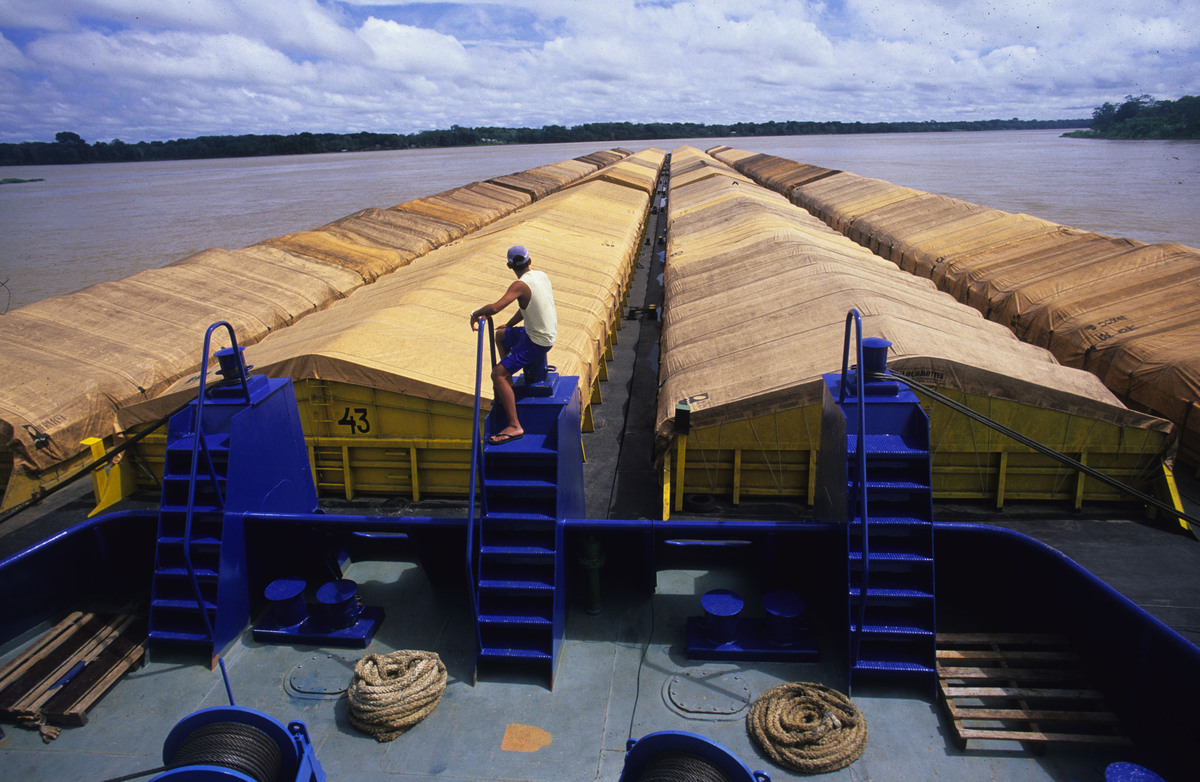A worker watches over giant soy barges docked on a wide brown river