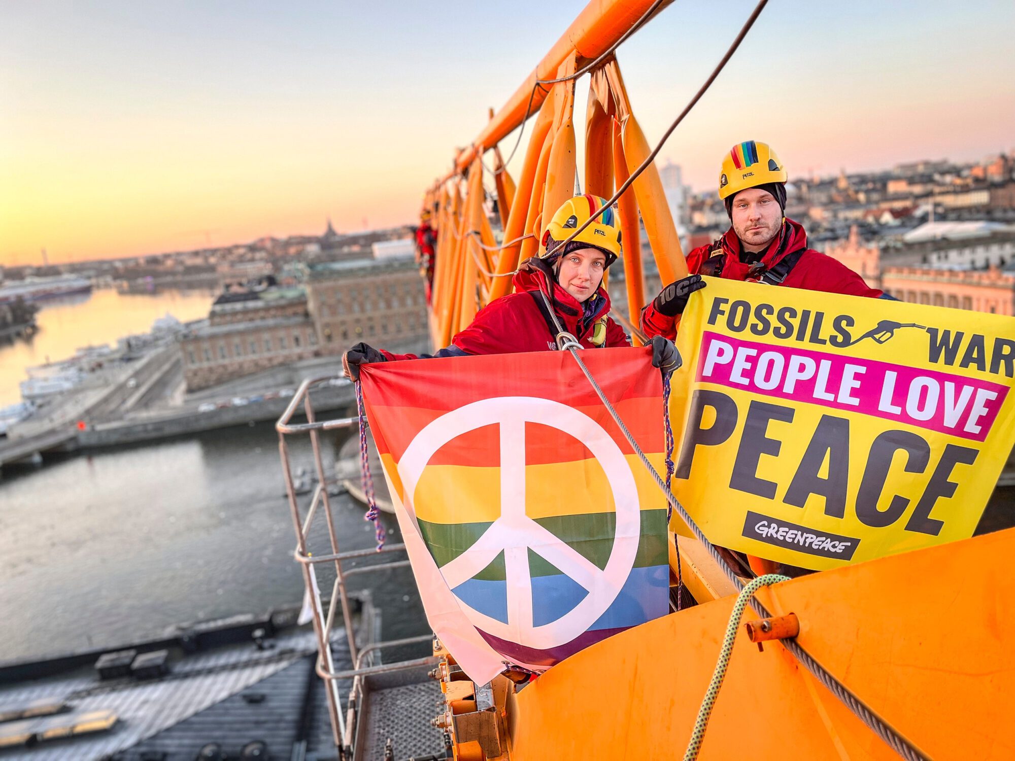 Two Greenpeace activists above a city flying a peace sign and “Fossils = war. People love peace” banners