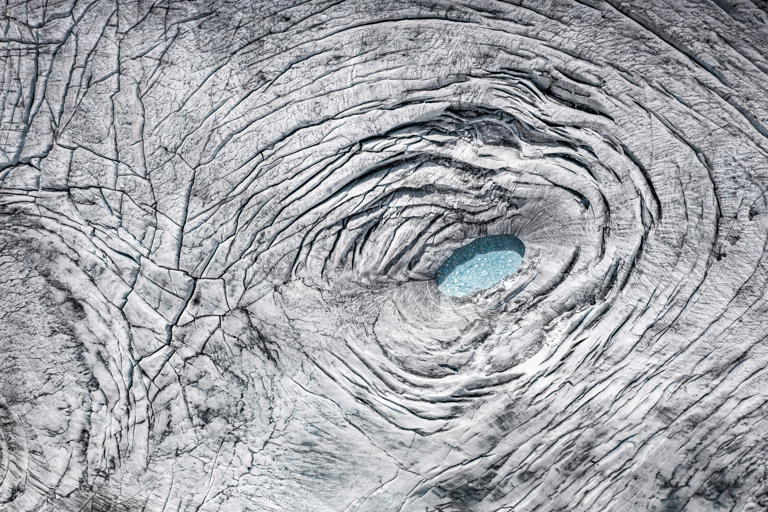 From above, a wrinkled glacier ice with a small water hole in the centre