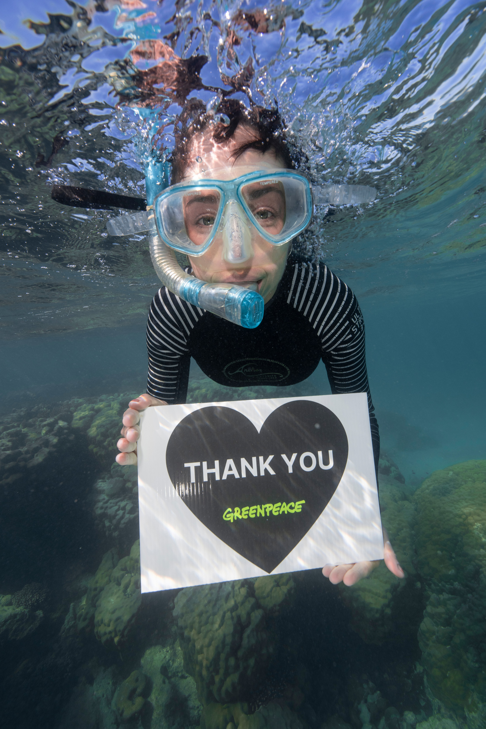 Greenpeace campaigner swims underwater with a snorkel and a sign that says “Thank you” in a heart.
