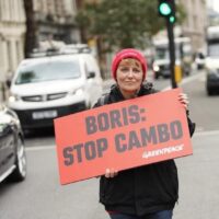 An activist stands in a road holding a sign that reads 'Boris: stop cambo'
