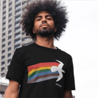 A model wears a black greenpeace tshirt with a rainbow design in an urban setting