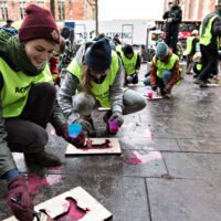 Activists stencil animal designs in pink on a wet pavement