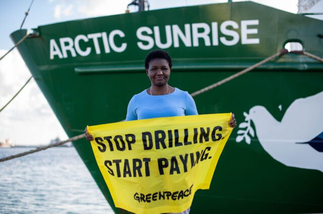 Victorine holds a banner in front of the Arctic Sunrise ship.