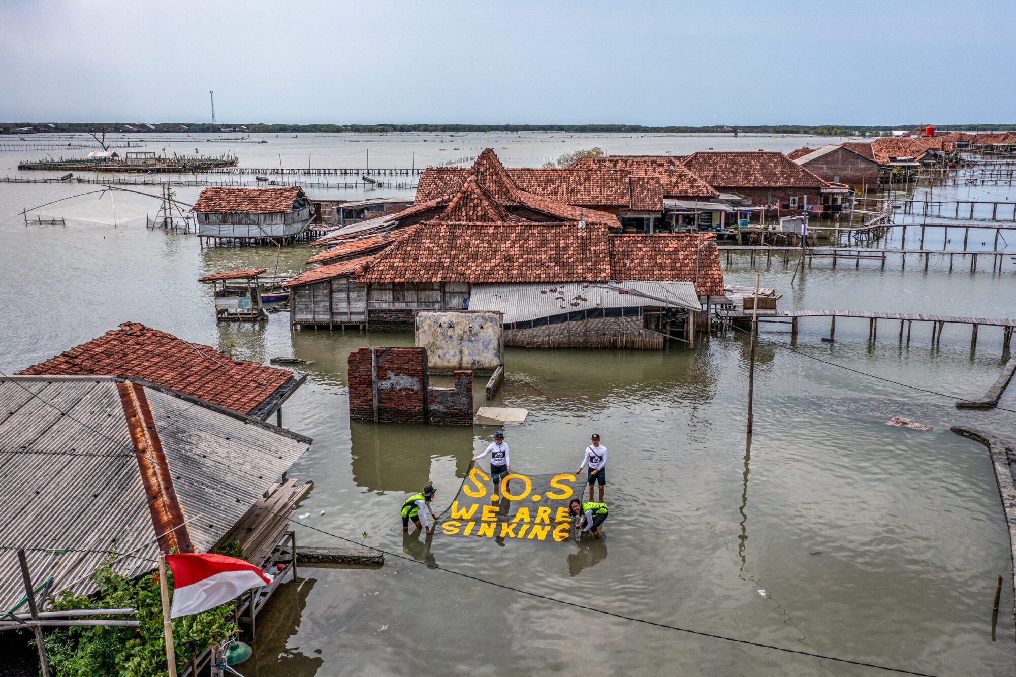 Red roofs poke from water in a submerged village, as campaigners stretch a banner reading "S.O.S we are sinking".